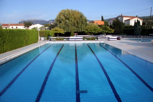 Piscine extérieure avec lignes de nage, eau turquoise et collines en arrière-plan ensoleillé calme.